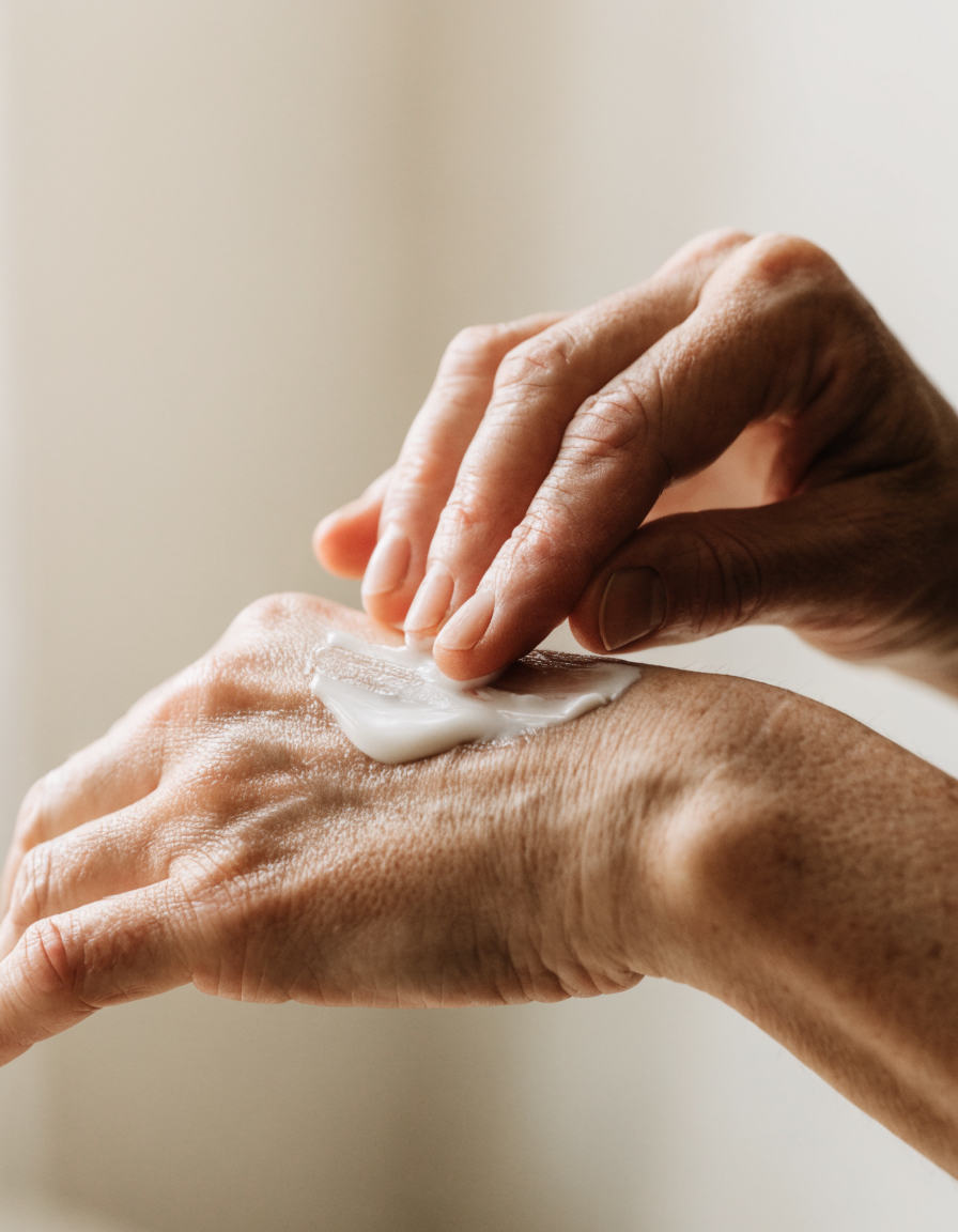 A tube of cream in one hand, being smoothed across the back of the other